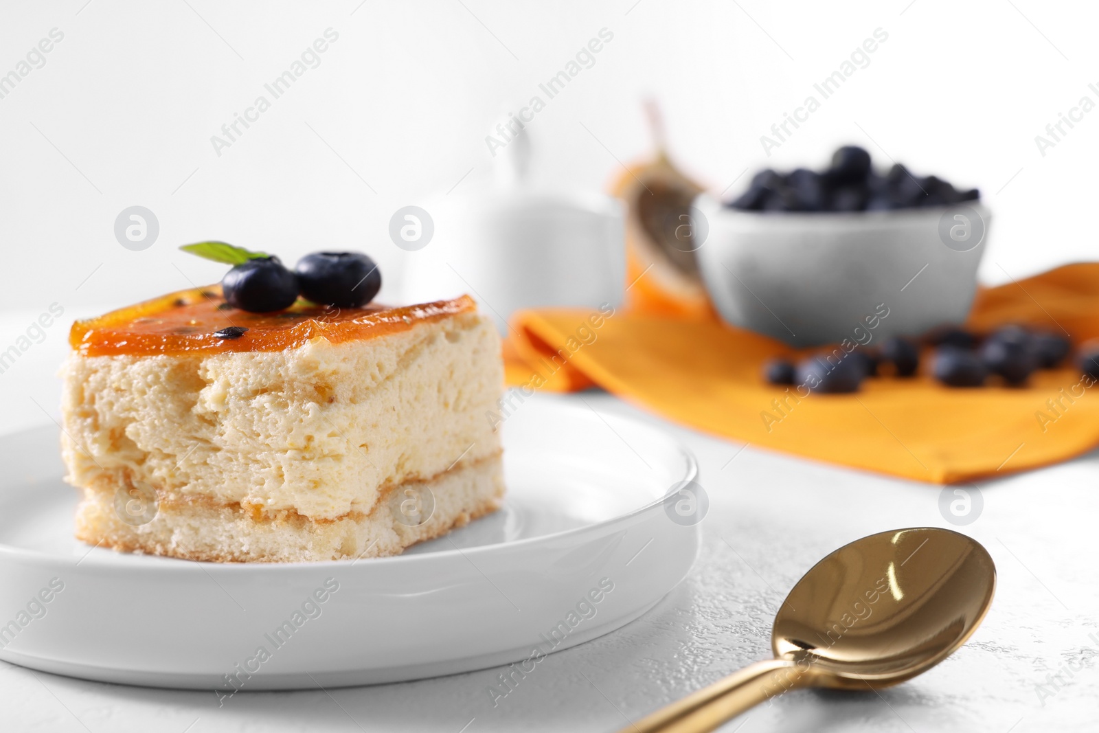 Photo of Piece of delicious cheesecake with blueberries and spoon on white table, closeup. Space for text