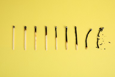 Photo of Different stages of burnt matches on yellow  background, flat lay