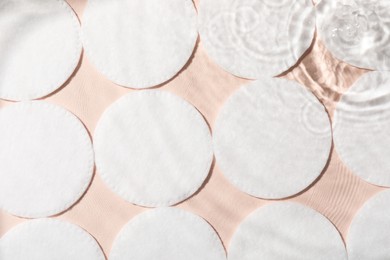 Many cotton pads in water on beige background, flat lay