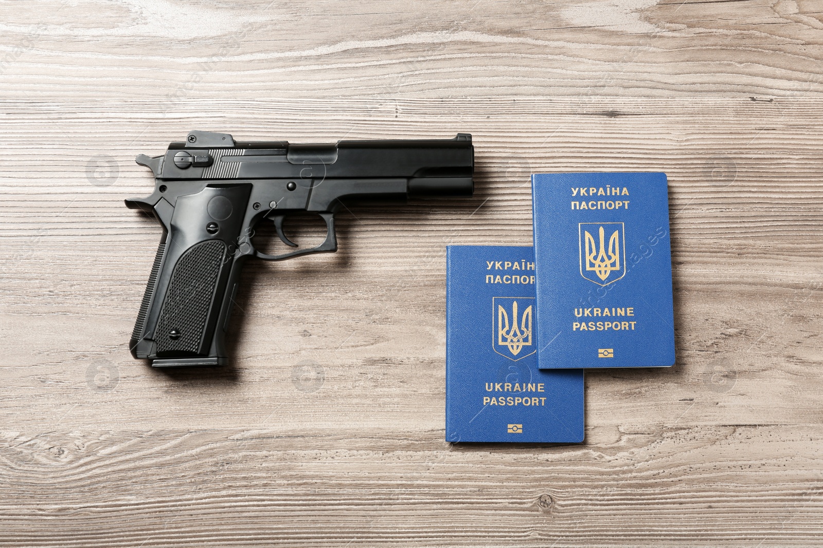 Photo of Gun with Ukrainian travel passports on wooden background, flat lay