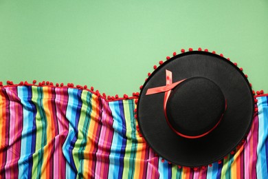 Photo of Mexican sombrero hat and colorful poncho on green background, flat lay. Space for text