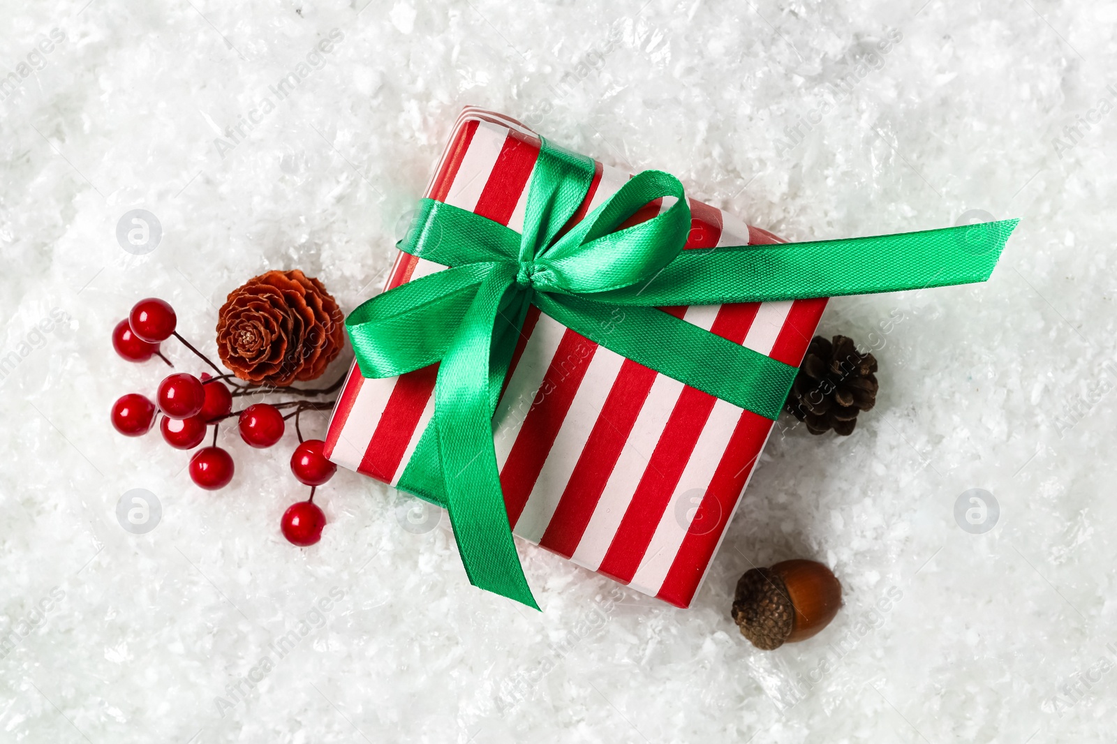 Photo of Christmas gift box with green bow and festive decor on snow, flat lay