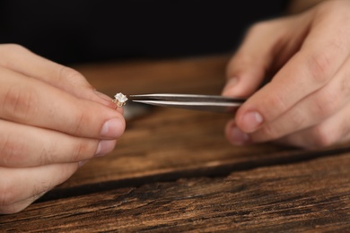 Photo of Male jeweler evaluating earring at table in workshop, closeup