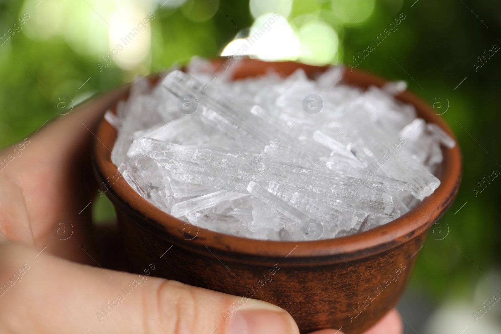 Photo of Woman holding bowl with menthol crystals against blurred background, closeup