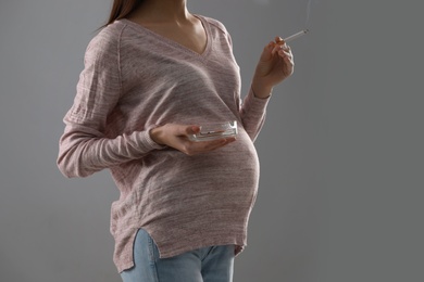 Photo of Young pregnant woman smoking cigarette on grey background. Space for text
