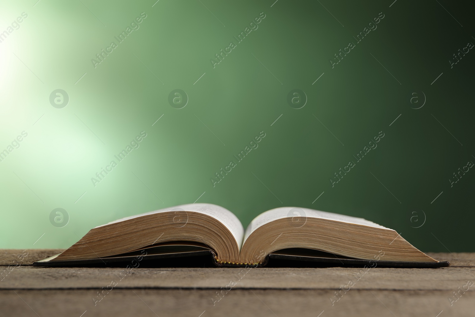 Photo of Open Bible on wooden table against green background. Space for text