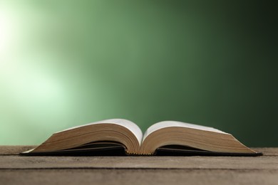 Open Bible on wooden table against green background. Space for text