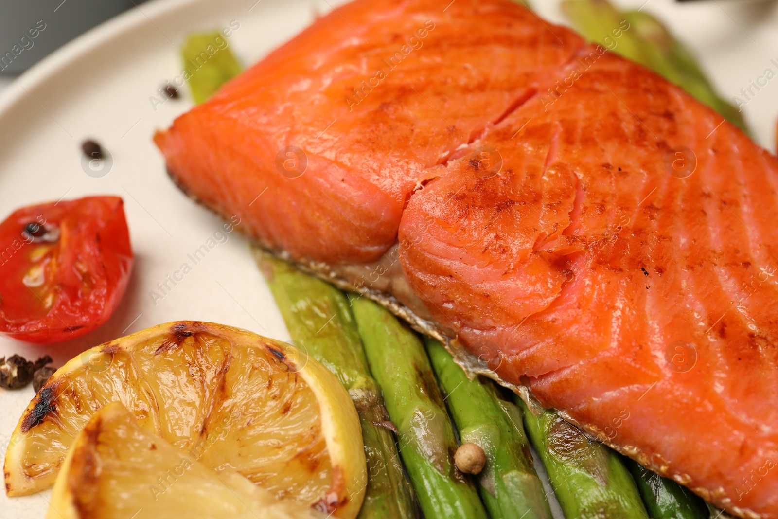 Photo of Tasty grilled salmon with asparagus, tomatoes and lemon on plate, closeup