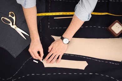 Photo of Tailor marking sewing pattern on fabric with chalk at table, top view