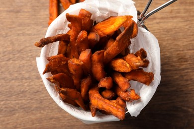 Photo of Frying basket with sweet potato fries on wooden table, closeup
