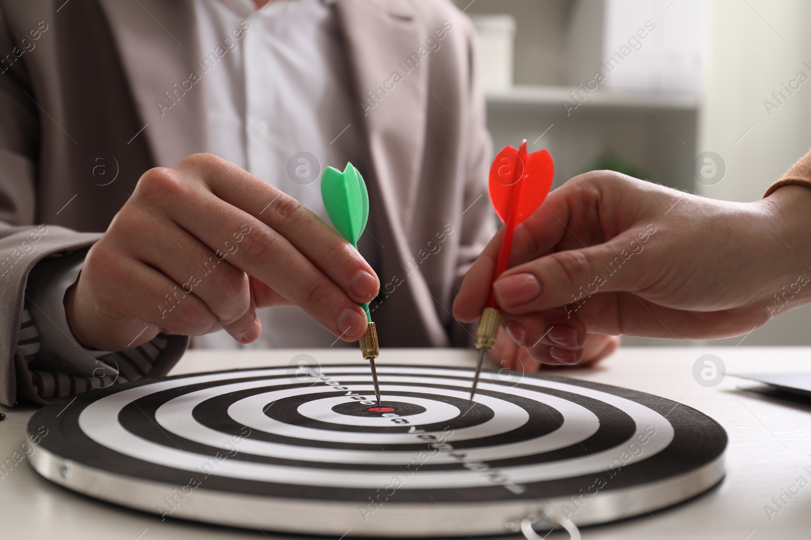 Photo of Business targeting concept. Man and woman with darts aiming at dartboard at table indoors, closeup