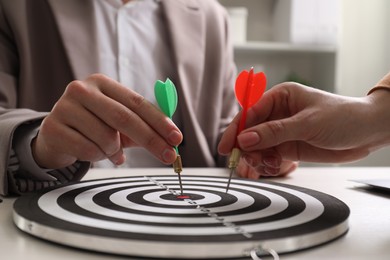 Photo of Business targeting concept. Man and woman with darts aiming at dartboard at table indoors, closeup