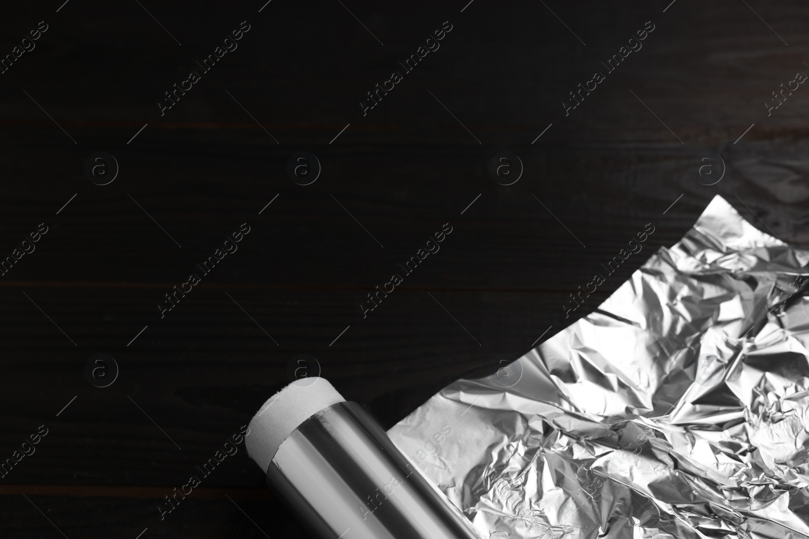 Photo of Roll of aluminum foil on dark wooden table, above view. Space for text