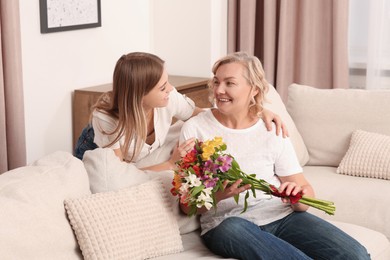 Photo of Young daughter congratulating her mom with flowers at home. Happy Mother's Day