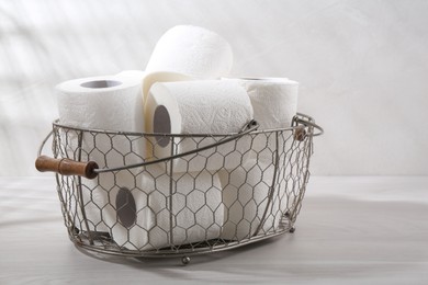 Photo of Soft toilet paper rolls in metal basket on white wooden table, closeup