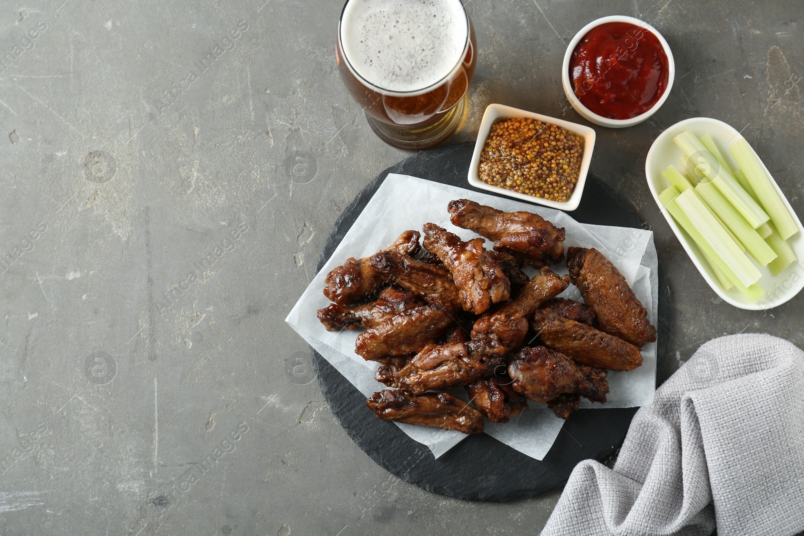 Photo of Delicious chicken wings served with beer on grey table, flat lay. Space for text