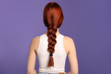Woman with red dyed braided hair on purple background, back view
