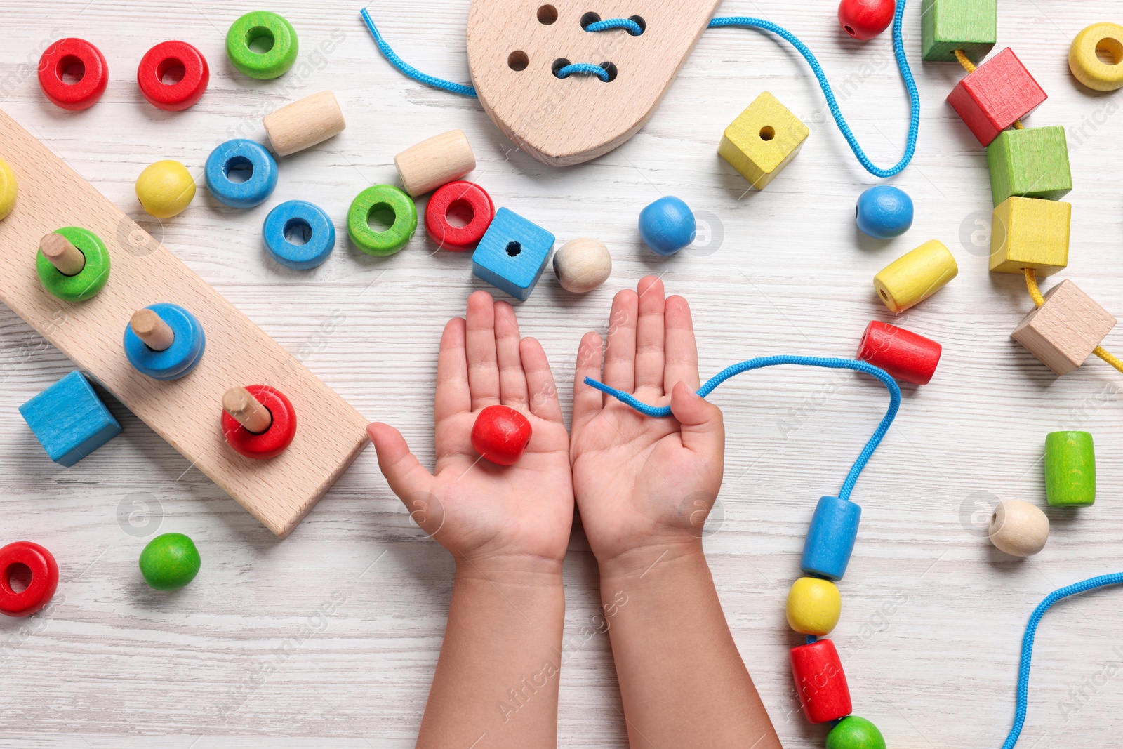 Photo of Motor skills development. Little child playing with wooden pieces and string for threading activity at white table, top view