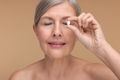 Beautiful woman with vitamin pill on beige background