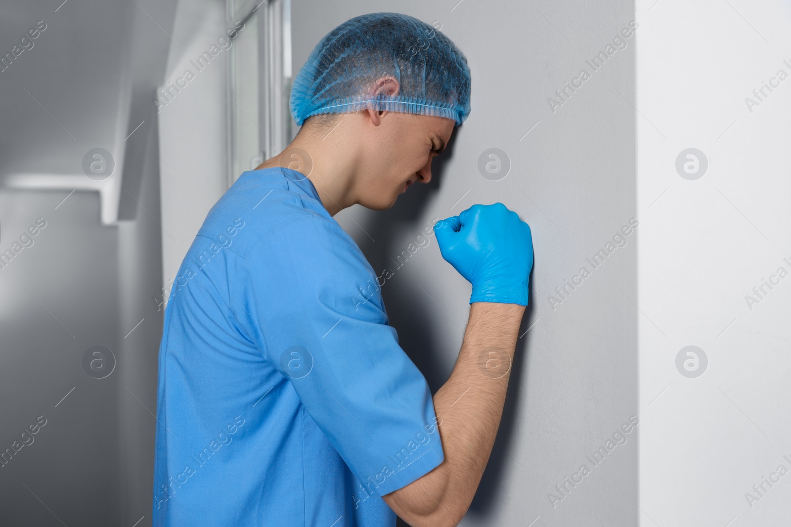 Photo of Stressed doctor near grey wall in hospital hallway