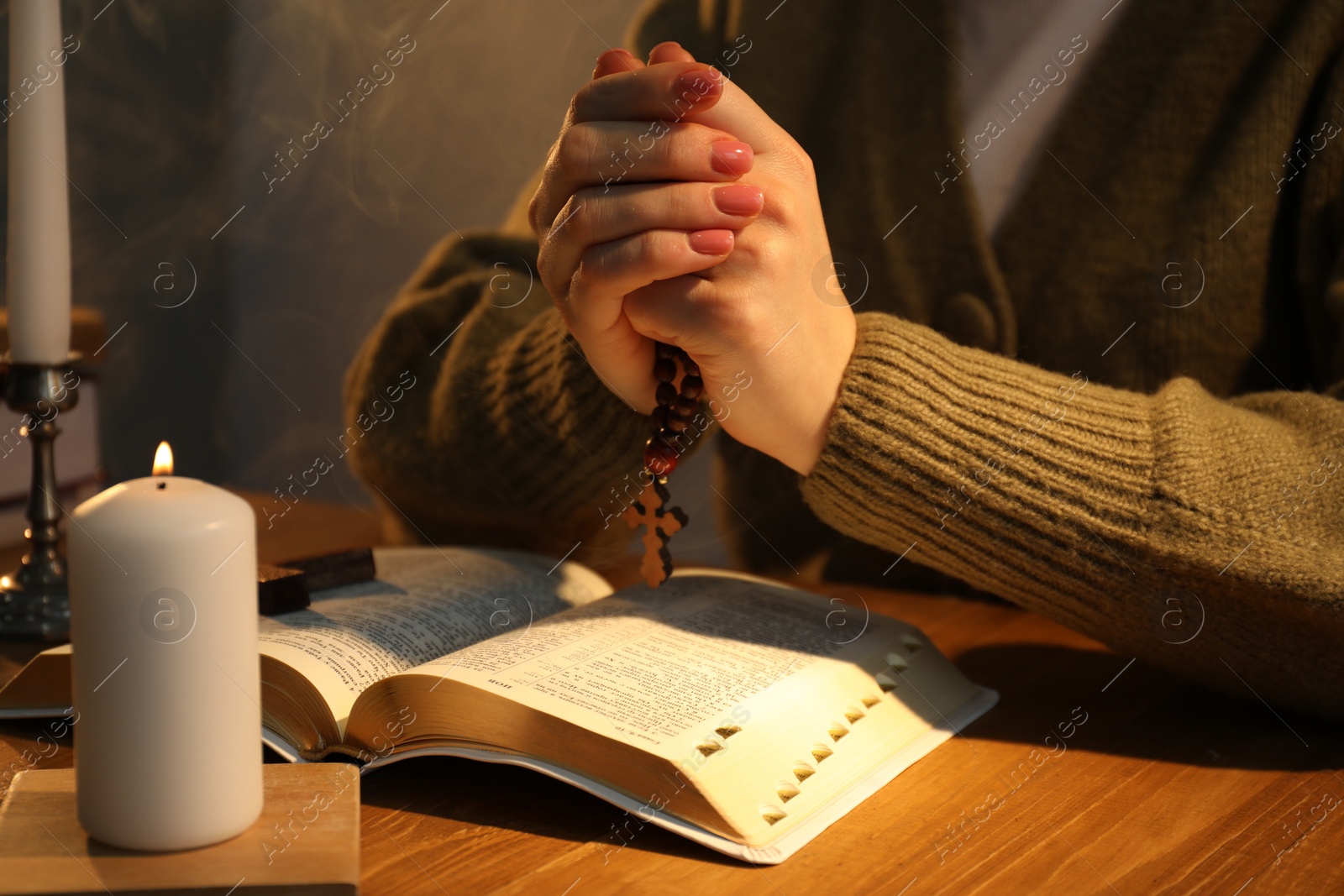 Photo of Woman praying at table with burning candle and Bible, closeup