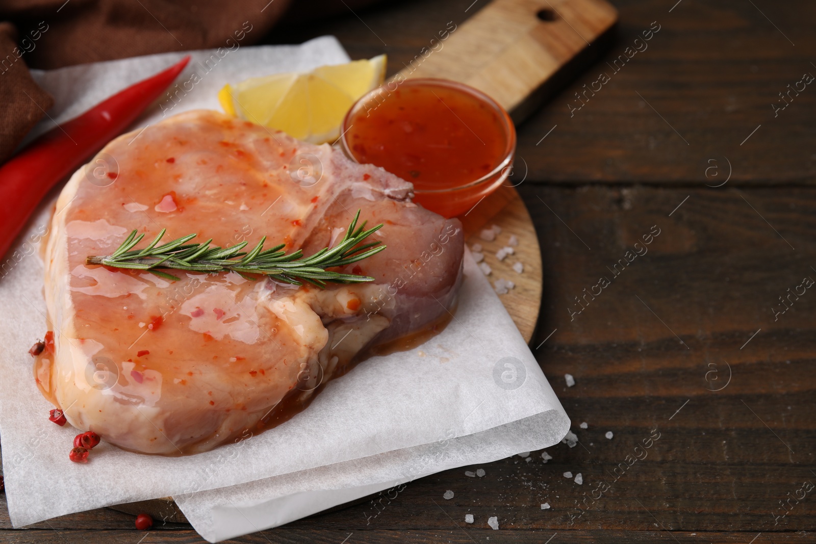Photo of Board with raw marinated meat, rosemary and spices on wooden table, closeup. Space for text