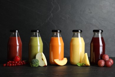 Photo of Bottles with delicious colorful juices and fresh ingredients on black table