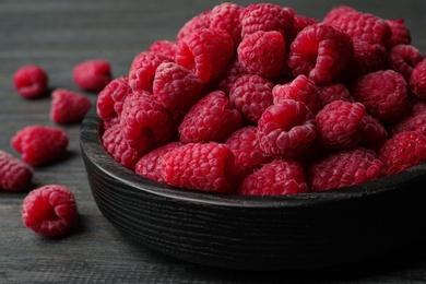 Bowl of delicious fresh ripe raspberries on dark wooden table, closeup view