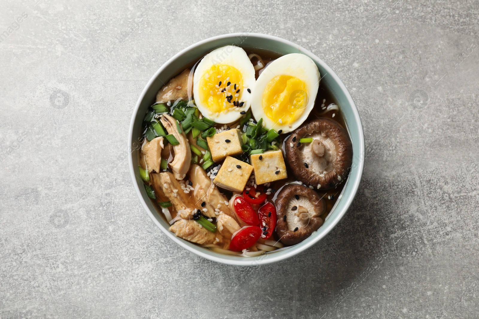 Photo of Bowl of delicious ramen on grey table, top view. Noodle soup