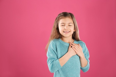 Portrait of girl holding hands near her heart on color background. Space for text