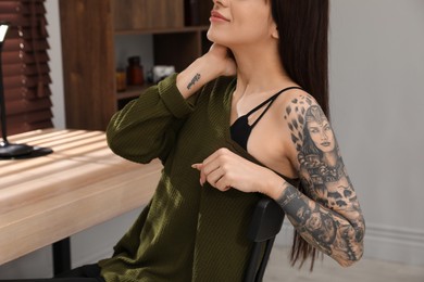 Photo of Beautiful woman with tattoos on arm at table indoors, closeup