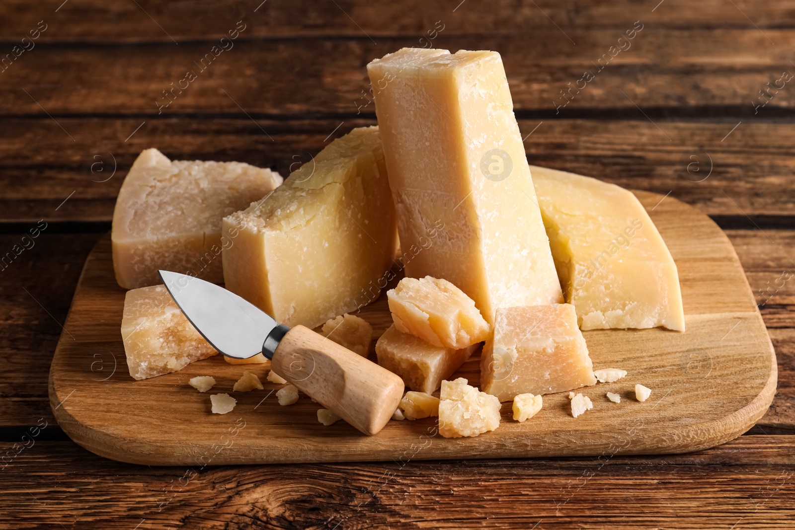 Photo of Parmesan cheese with board and knife on wooden table