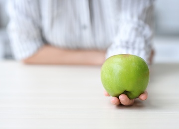 Photo of Woman holding ripe green apple at table