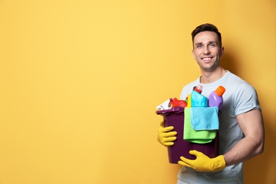 Man with bucket of detergents on color background. Space for text