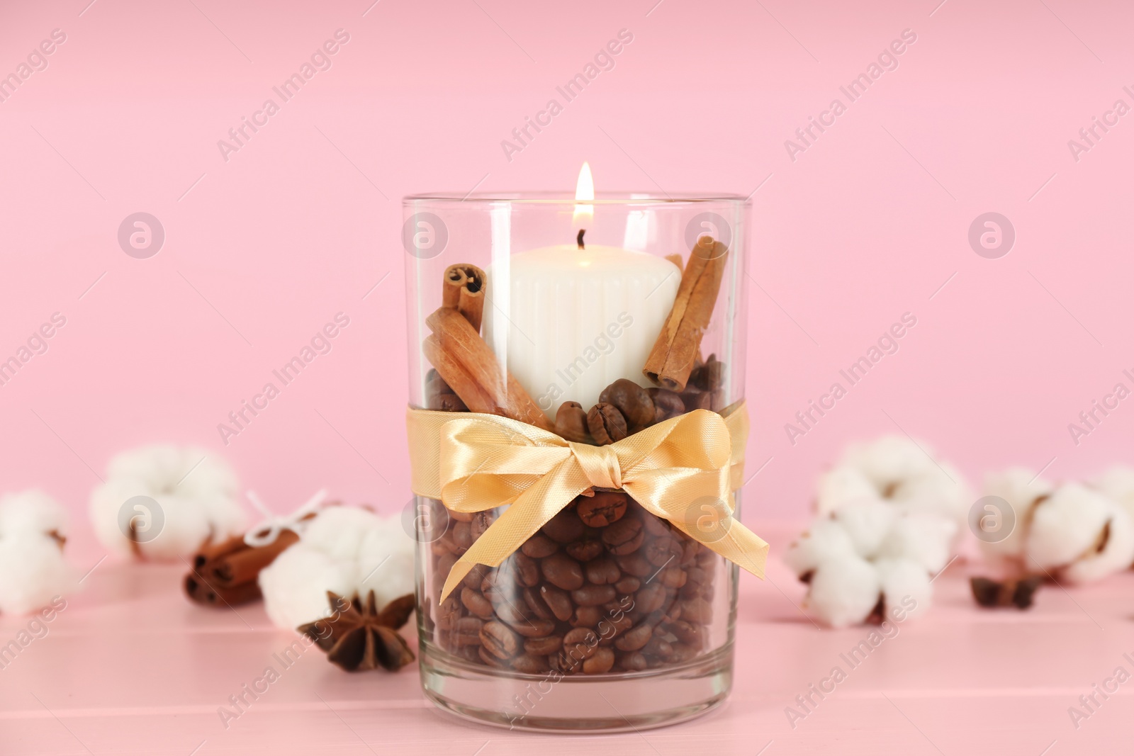 Photo of Glass holder with burning candle, coffee beans and cinnamon on pink wooden table, closeup