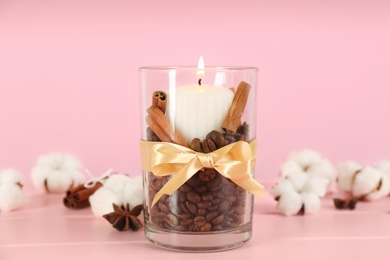Photo of Glass holder with burning candle, coffee beans and cinnamon on pink wooden table, closeup