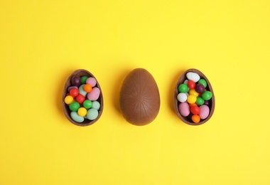 Photo of Tasty chocolate eggs with colorful candies on yellow background, flat lay