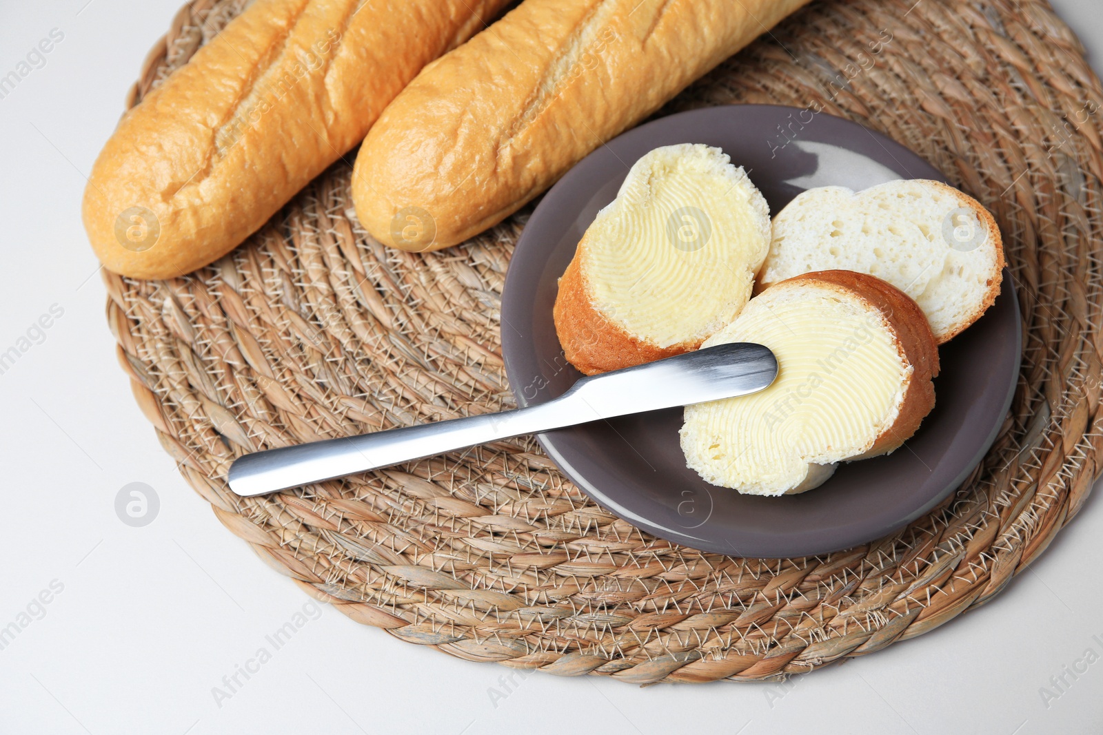 Photo of Whole and cut baguettes with fresh butter on white table, above view