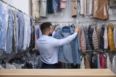 Dry-cleaning service. Worker holding denim shirt indoors