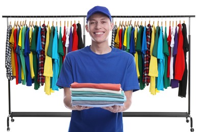 Image of Dry-cleaning delivery. Happy courier holding folded clothes near wardrobe racks on white background