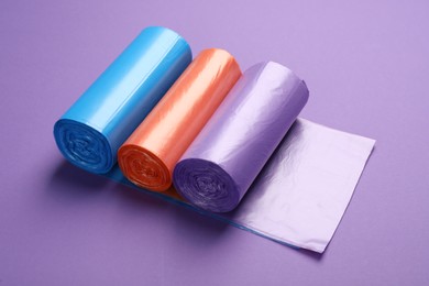 Photo of Rolls of different color garbage bags on violet background