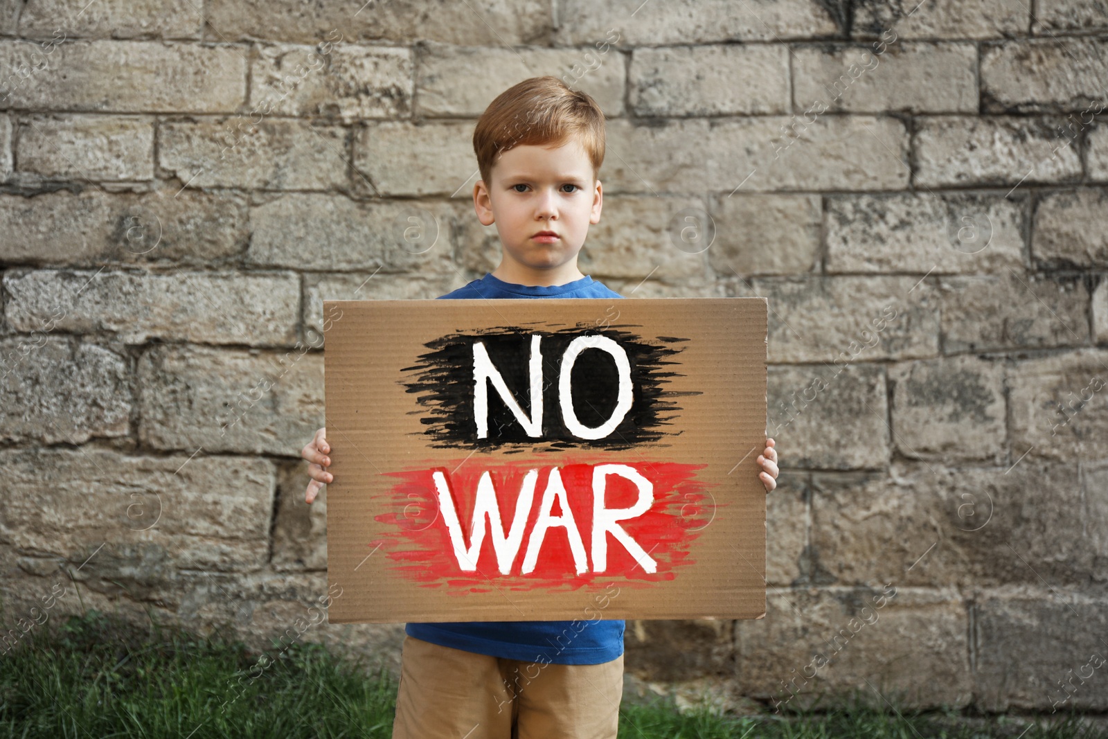 Photo of Sad boy holding poster with words No War against brick wall outdoors