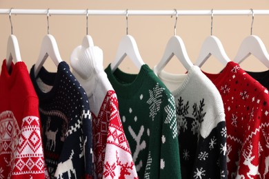 Rack with different Christmas sweaters on beige background, closeup
