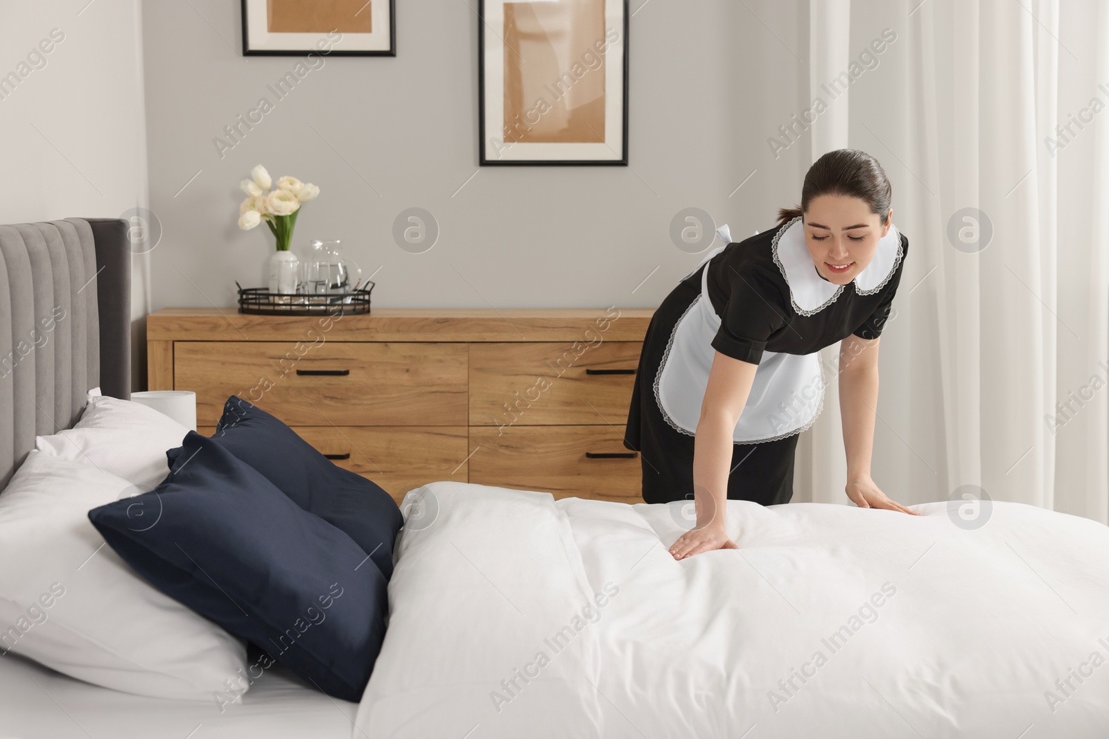 Photo of Young chambermaid making bed in hotel room