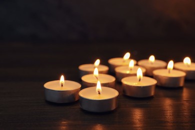 Many burning candles on wooden table, closeup