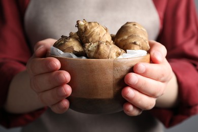 Woman holding bowl with Jerusalem artichokes on light grey background, closeup