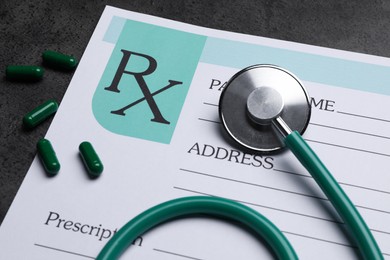 Photo of Medical prescription form, stethoscope and pills on dark grey table, closeup