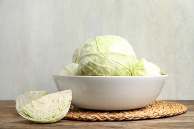 Photo of Fresh whole and cut cabbages in bowl on wooden table