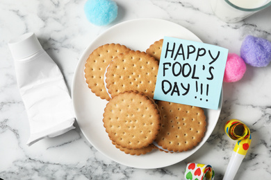 Photo of Cookies with toothpaste and HAPPY FOOL'S DAY note on white marble table, flat lay. April holiday