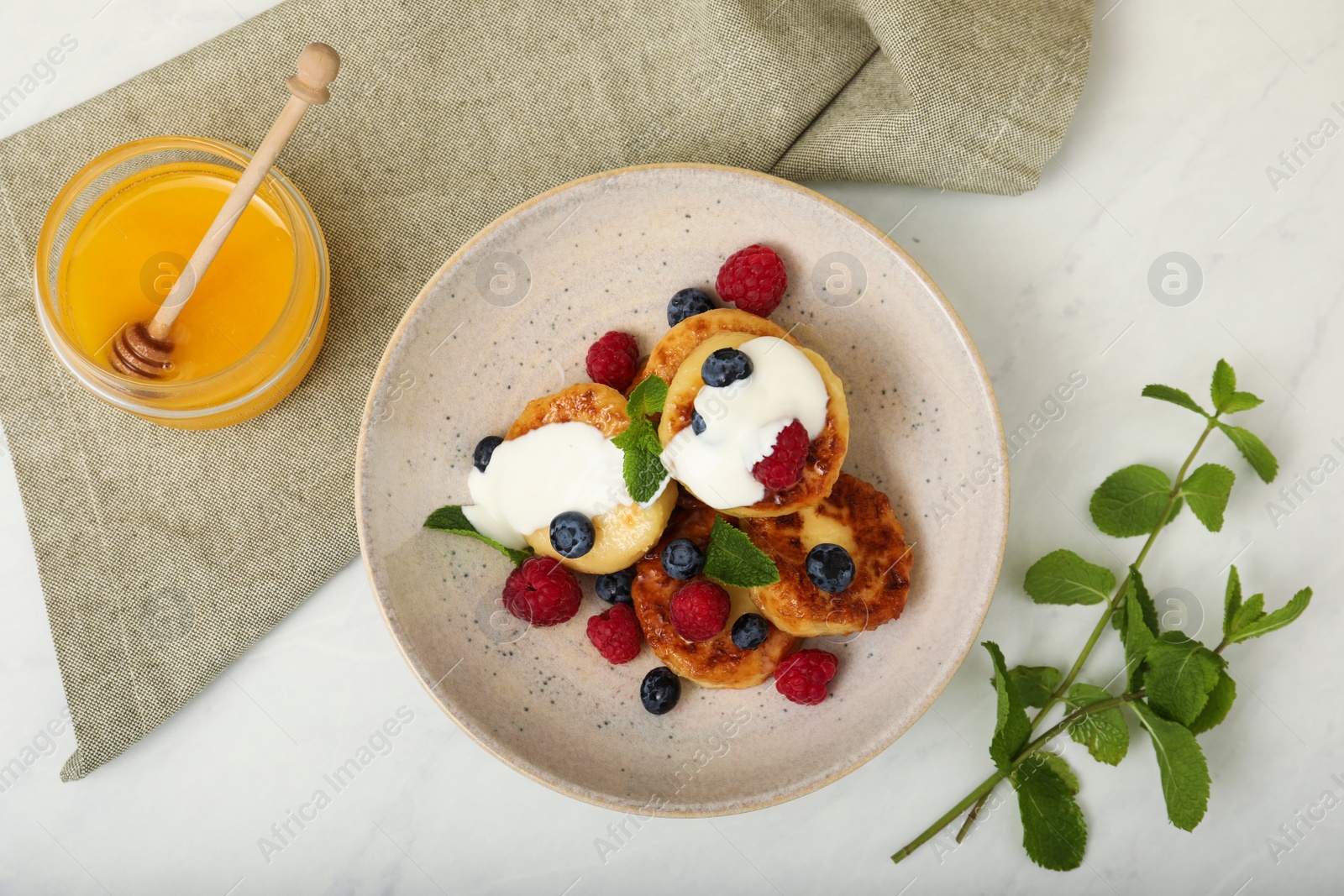 Photo of Delicious cottage cheese pancakes with fresh raspberries, sour cream and mint served on white table, flat lay